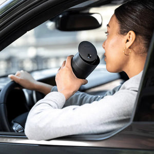 Persoun drénkt Kaffi aus schwaarzer Thermosbecher mat Schiebelidd am Auto, Deel vun Take away, Fellow, EspressoGear, alles iwwer Kaffi.