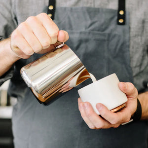 Barista schëtt Mëllech aus enger poléierter Kanne aus Edelstahl, Deel vun den Espresso Accessoiren a vun der Mëllechkanne, alles ëm de Kaffi.