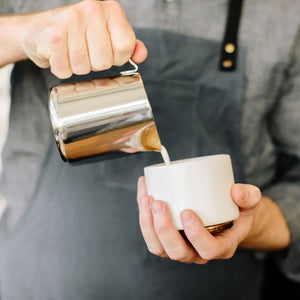 Barista schëtt Mëllech aus enger poléierter Kanne aus Edelstahl, Deel vun den Espresso Accessoiren a vun der Mëllechkanne, alles ëm de Kaffi.