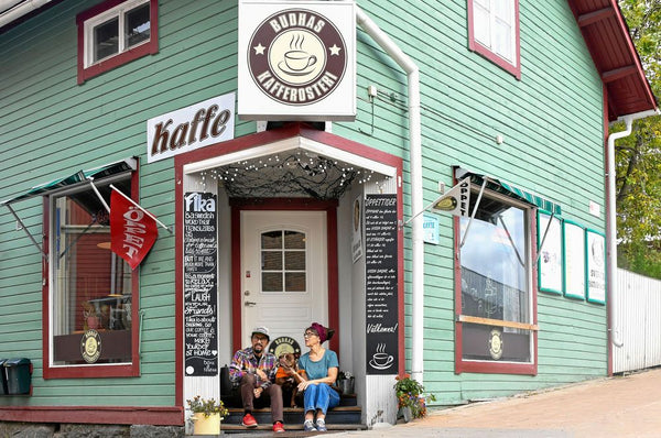 Grön träbyggnad med skylt för kaffebryggeri och två personer sittande på trappan vid entrén.