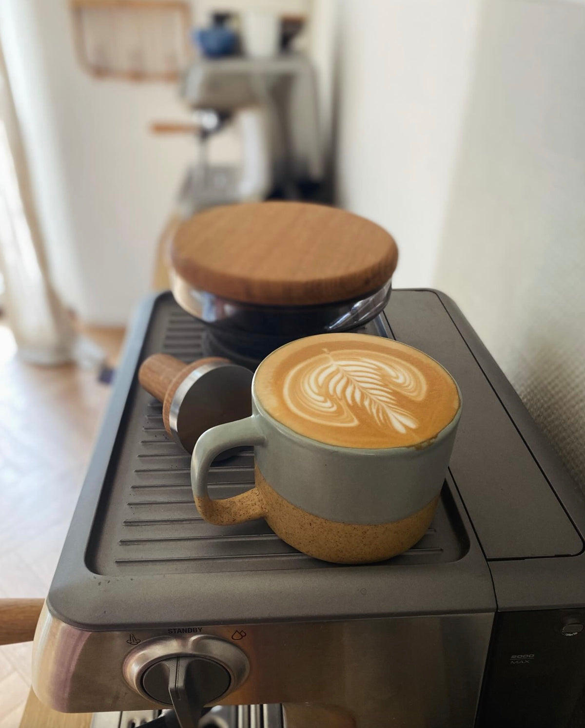 Espressomaskin med en cappuccino i kopp dekorerad med latte art på en köksbänk.