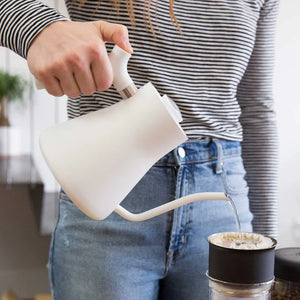 Hand, déi Waasser aus engem wäisse Waasserkach mat schmolem Ausgoss an e Kaffisfilter schëddt, Deel vun EspressoGear, alles iwwer Kaffi.