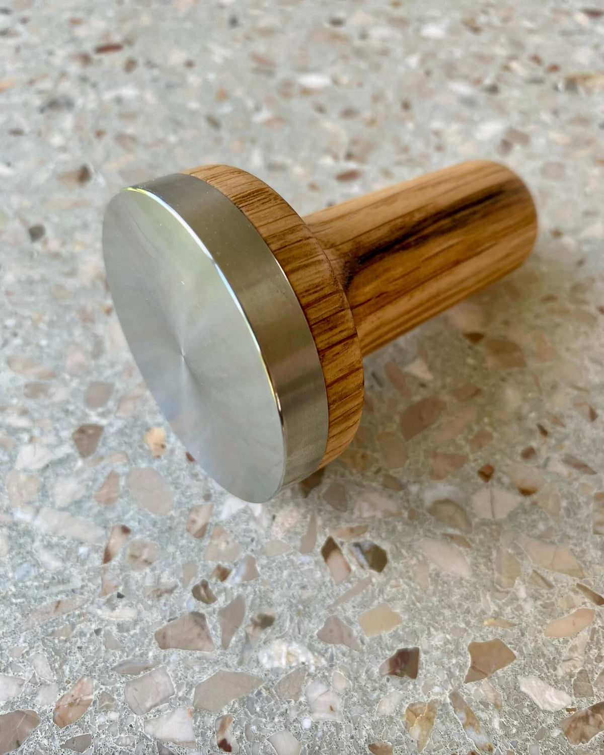 Espressotamper med handtag i trä och bas i rostfritt stål på marmoryta.