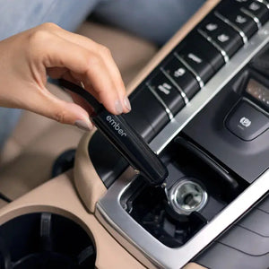Hand, déi den Autolueder fir den Ember elektresche Becher am Zigarettestecker vum Auto uschléisst, fir eng komfortabel Opluedung.